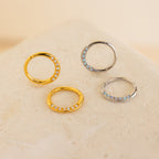 Two gold and two silver Opal Cartilage Huggies with small embedded stones, ideal for helix piercings, displayed on a light textured surface.