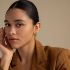 Woman wearing a brown pinstripe blazer and Herkimer Diamond Threader Earrings, gazing at the camera with her hand on her face.