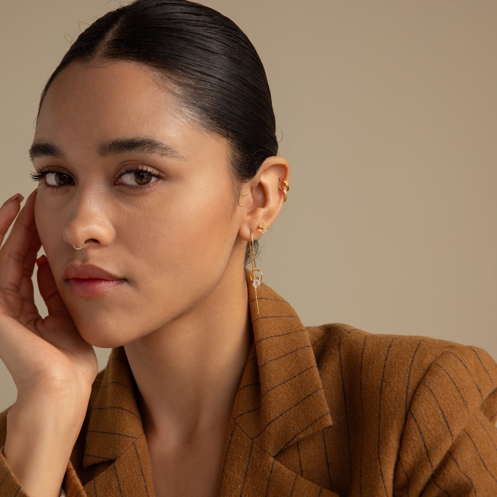 Woman wearing a brown pinstripe blazer and Herkimer Diamond Threader Earrings, gazing at the camera with her hand on her face.