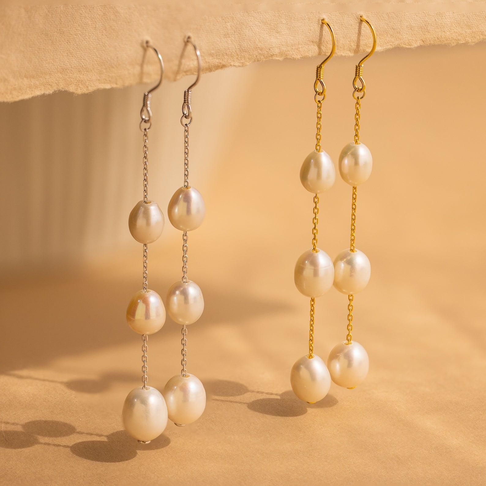 Close-up of two Long Pearl Dangle Earrings in Gold and Silver. 