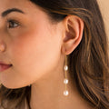 Close-up of model wearing long gold pearl chain earrings.