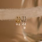 Close-up of Gold and Silver Dainty Pearl Huggies hanging on a beige fabric. 