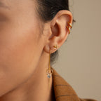 Close-up of a woman’s ear adorned with three gold earrings: a cuff, a stud, and elegant Herkimer Diamond Threader Earrings.