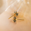 A pair of Herkimer Agate Studs featuring gold geometric faceted translucent stones is displayed on a soft, beige marble surface.