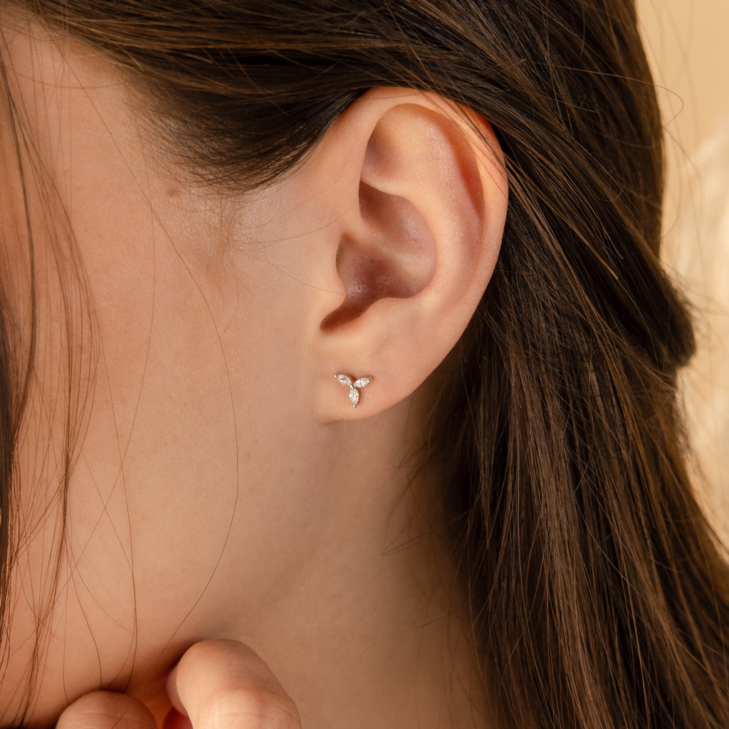 Close-up of a woman’s ear wearing the Trio Floral Marquise Studs, a gold set featuring three small stones.