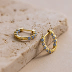 Inside Out Ivy Huggies featuring light blue gemstones are displayed on a textured beige stone surface.