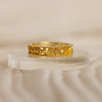The Filigree Flower Ring features a gold band with intricate scrollwork and small embedded diamonds, evoking vintage charm and displayed elegantly on a clear, curved stand.