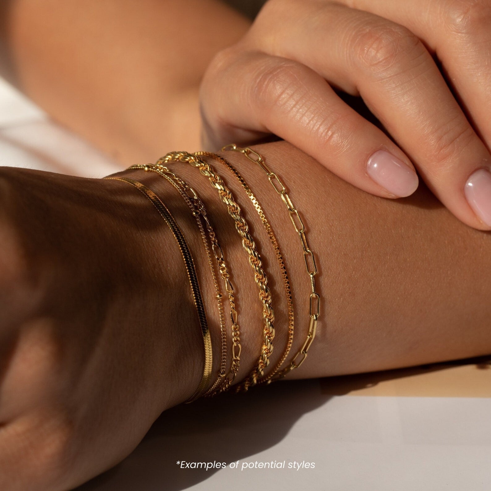 A close-up of a wrist wearing multiple Mystery Bracelets highlights their delicate gold design and subtle shimmer, adding sophistication alongside manicured hands.