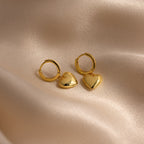 Puff Heart Charm Huggies are displayed on a soft, beige satin fabric background.