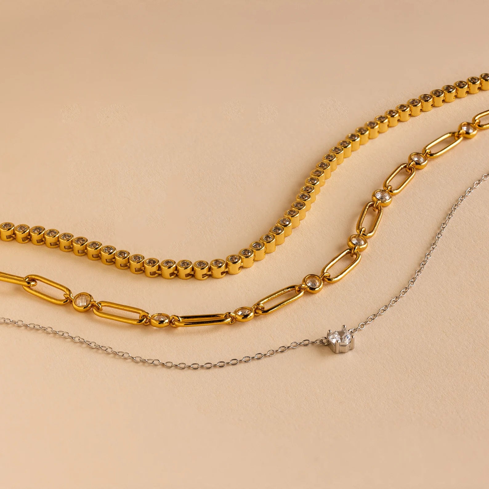 Three necklaces from the Mystery Necklace Box on a beige background: two gold chains and one delicate silver chain with a small pendant—ideal for your jewelry collection or as a special surprise.
