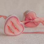 Two gold rings with gemstones sit in a Pink Velvet Heart Ring Box, radiating coquette charm, while another jewelry case is softly blurred in the background.
