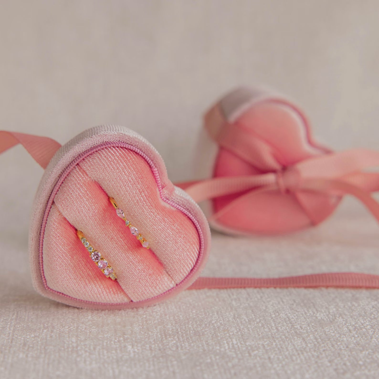 Two gold rings with gemstones sit in a Pink Velvet Heart Ring Box, radiating coquette charm, while another jewelry case is softly blurred in the background.
