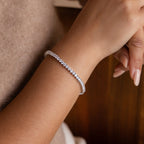 A woman's hand with nude manicured nails wears the 3-Prong Diamond Tennis Necklace & Bracelet Set in White Gold, showcasing its delicate sparkle and elegant design.