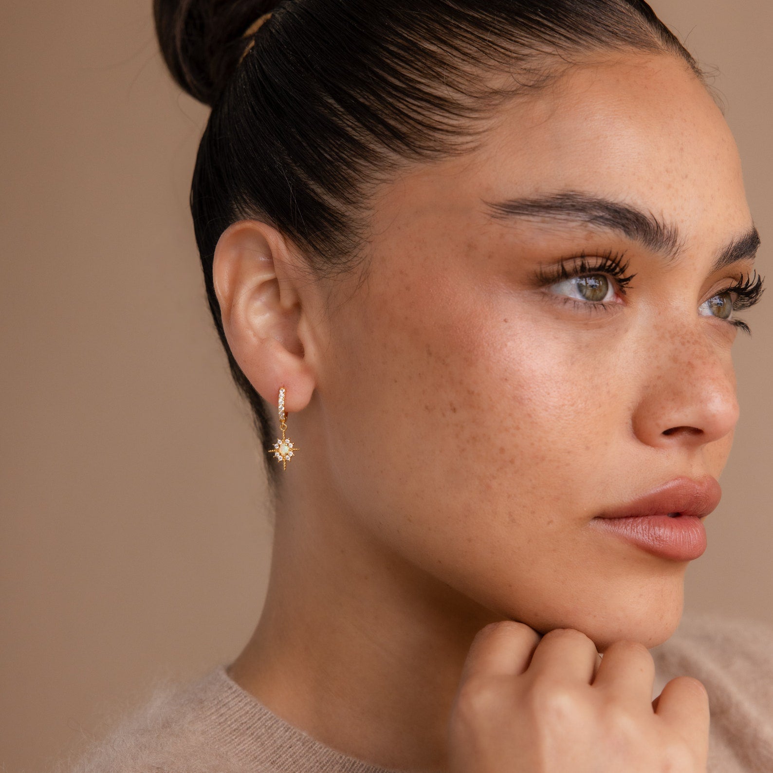Woman with smooth skin and freckles wears a gold hoop earring and the Opal Star Necklace & Earrings Set in 18K Gold, gazing thoughtfully to the side.