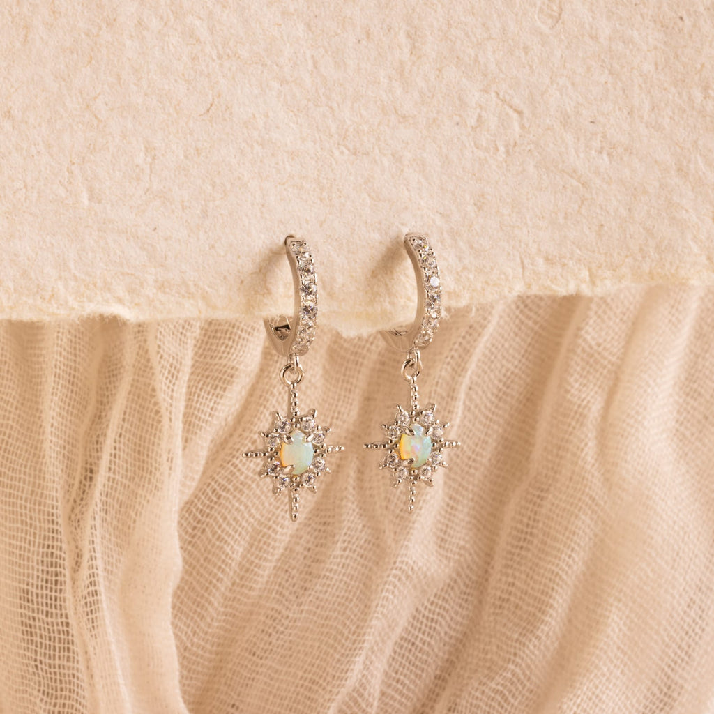 The Opal Star Necklace & Earrings Set in Silver, featuring sparkling accents, is displayed on textured cream fabric—an elegant pairing for your favorite looks.