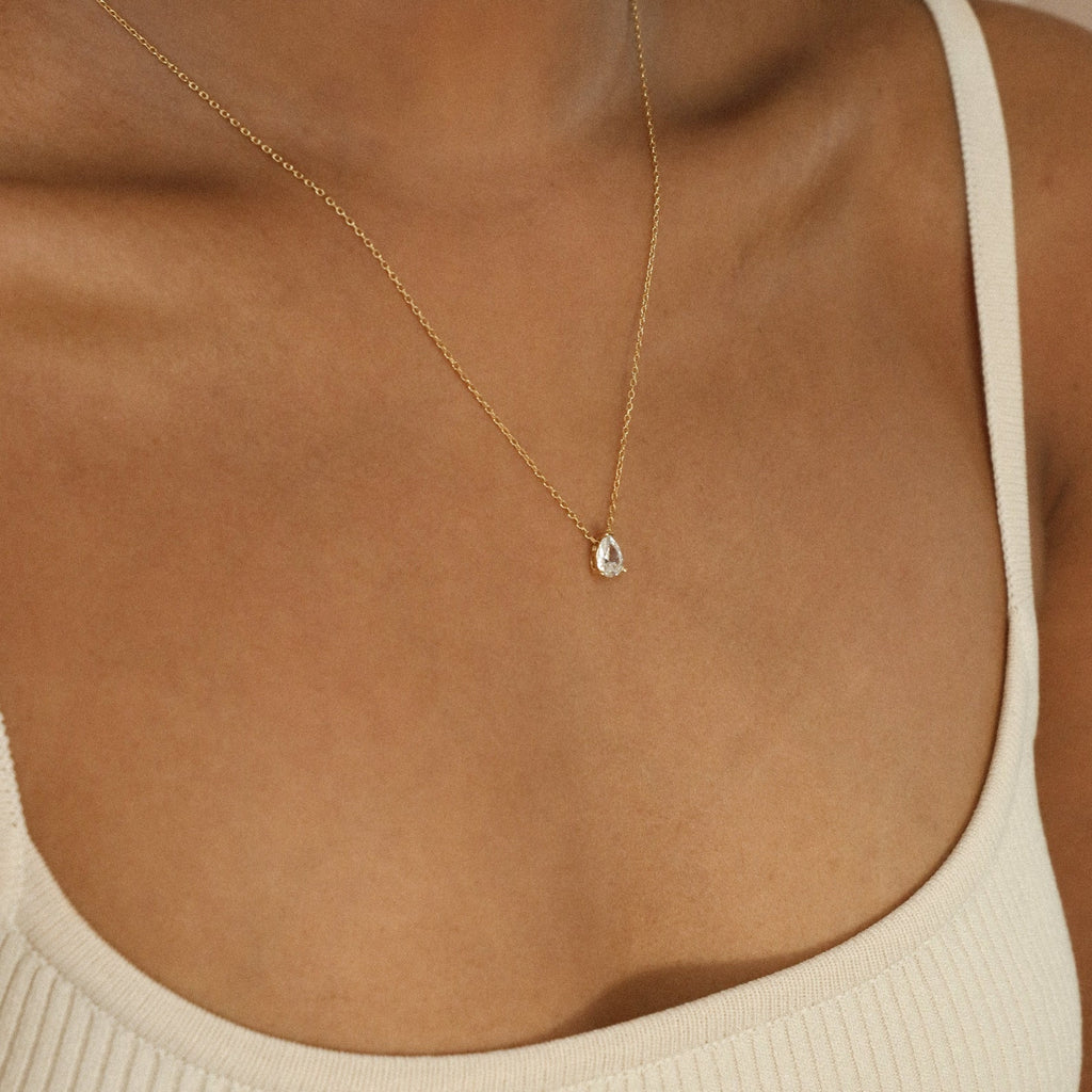 A person wearing a cream-colored tank top and the Dainty Diamond Necklace Set, featuring a delicate 925 Sterling Silver chain with a small teardrop-shaped pendant.