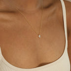 A person wearing a cream-colored tank top and the Dainty Diamond Necklace Set, featuring a delicate 925 Sterling Silver chain with a small teardrop-shaped pendant.
