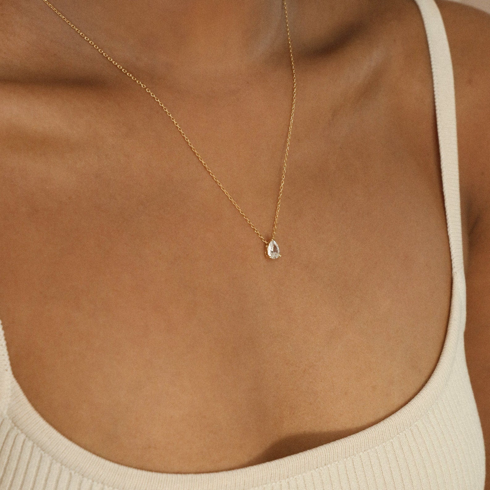 A person wearing a cream-colored tank top and the Dainty Diamond Necklace Set, featuring a delicate 925 Sterling Silver chain with a small teardrop-shaped pendant.