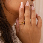 A person with manicured nails wears three stacked gold rings from the Opal Inlay Rings Set, featuring striking opal details and indigo blue accents.