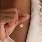 A person holds a Baby Handprint Coin Necklace—a gold pendant engraved with tiny handprints—making it a perfect personalized keepsake and thoughtful gift for new moms.