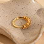 A gold ring with amber-colored beads, secured by a Ring Size Adjuster, rests on a speckled ceramic dish.