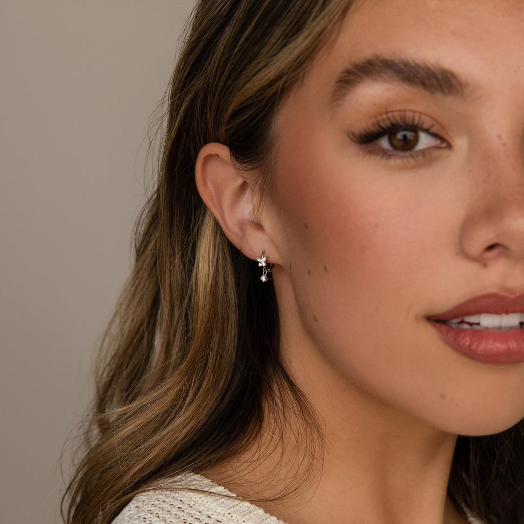 Close-up of a woman with wavy brown hair wearing soft makeup and the Diamond Butterfly Drop Jewelry Set in Sterling Silver—dangling star-shaped earrings and a sparkling butterfly drop necklace add an elegant touch.