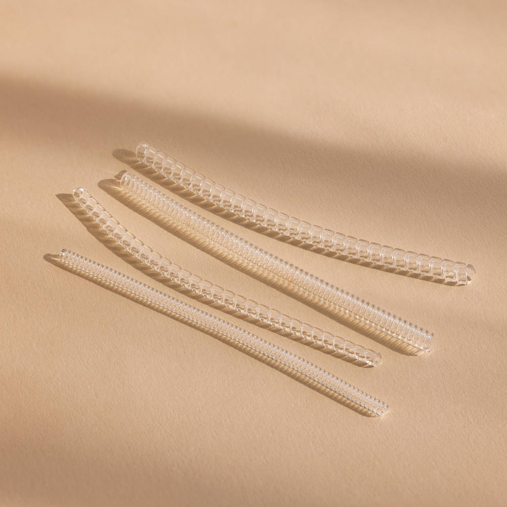 Four transparent, coiled Ring Size Adjusters are arranged diagonally on a beige surface under soft lighting.