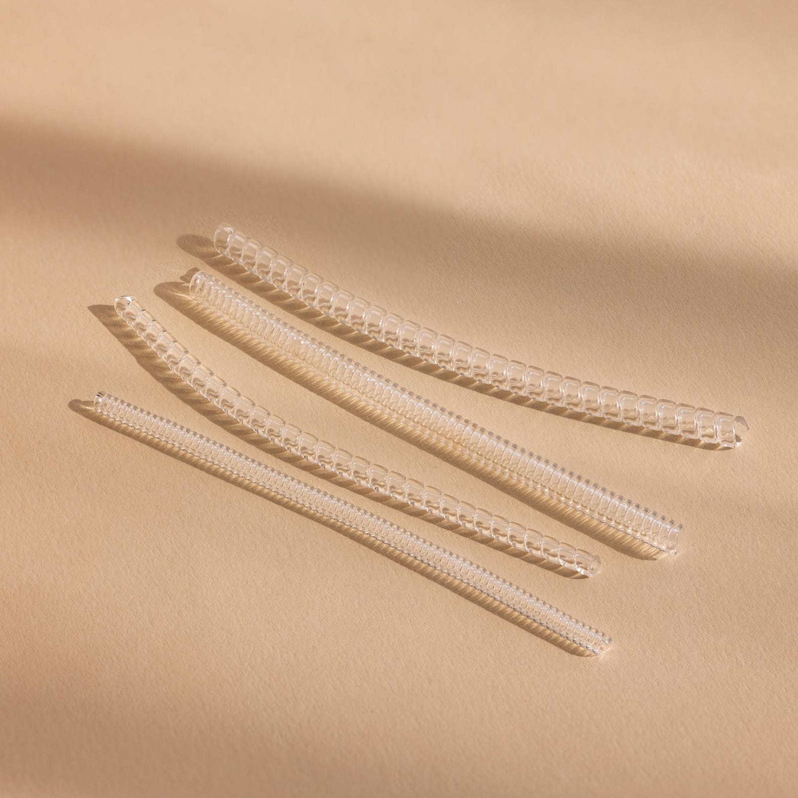 Four transparent, coiled Ring Size Adjusters are arranged diagonally on a beige surface under soft lighting.
