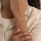 A person wears the Toi et Moi Birthstone Bracelet, which features a slim silver band and a customizable rectangular birthstone gem on their wrist.