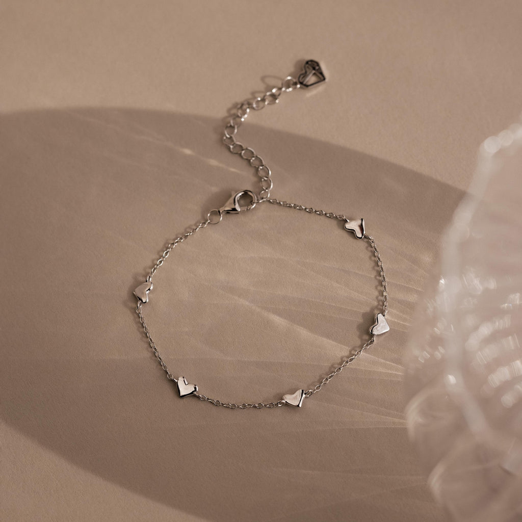 Elegant Heart Station Necklace & Bracelet Set in Sterling Silver, featuring small heart charms, displayed on a beige surface with soft shadows.