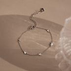 Elegant Heart Station Necklace & Bracelet Set in Sterling Silver, featuring small heart charms, displayed on a beige surface with soft shadows.