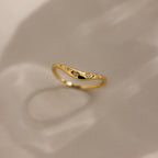 The North Star Curve Dome Ring features diamond star accents and delicate star-shaped engravings, with gemstones shimmering as it casts a soft shadow on a beige surface.