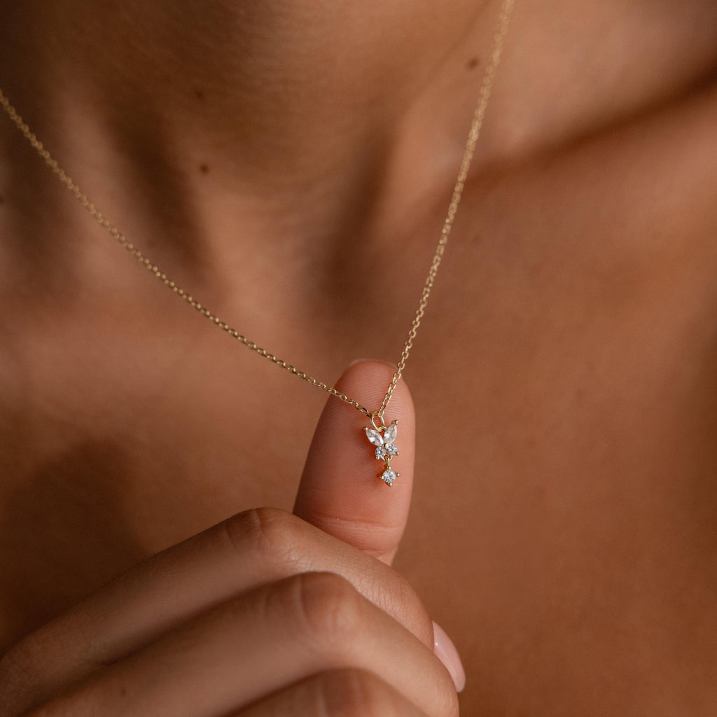 A hand holds the Diamond Butterfly Drop Jewelry Set in 18K Gold, featuring a sparkling butterfly pendant near a woman's neck—a charming bridesmaid gift.