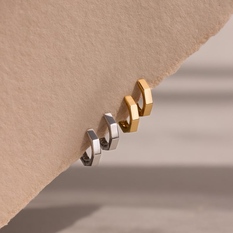 Two pairs of gold and silver geometric hoop earrings on a beige background