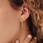 Close-up of a woman's ear wearing Editor Huggies in Rose Gold—one small hoop and one with a delicate hanging chain—highlighting minimal, classic jewelry style.