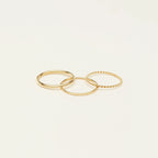 The Thin Stacking Rings Set in 18K Gold features three textured rings, ideal for creating a chic layered look on any light background.