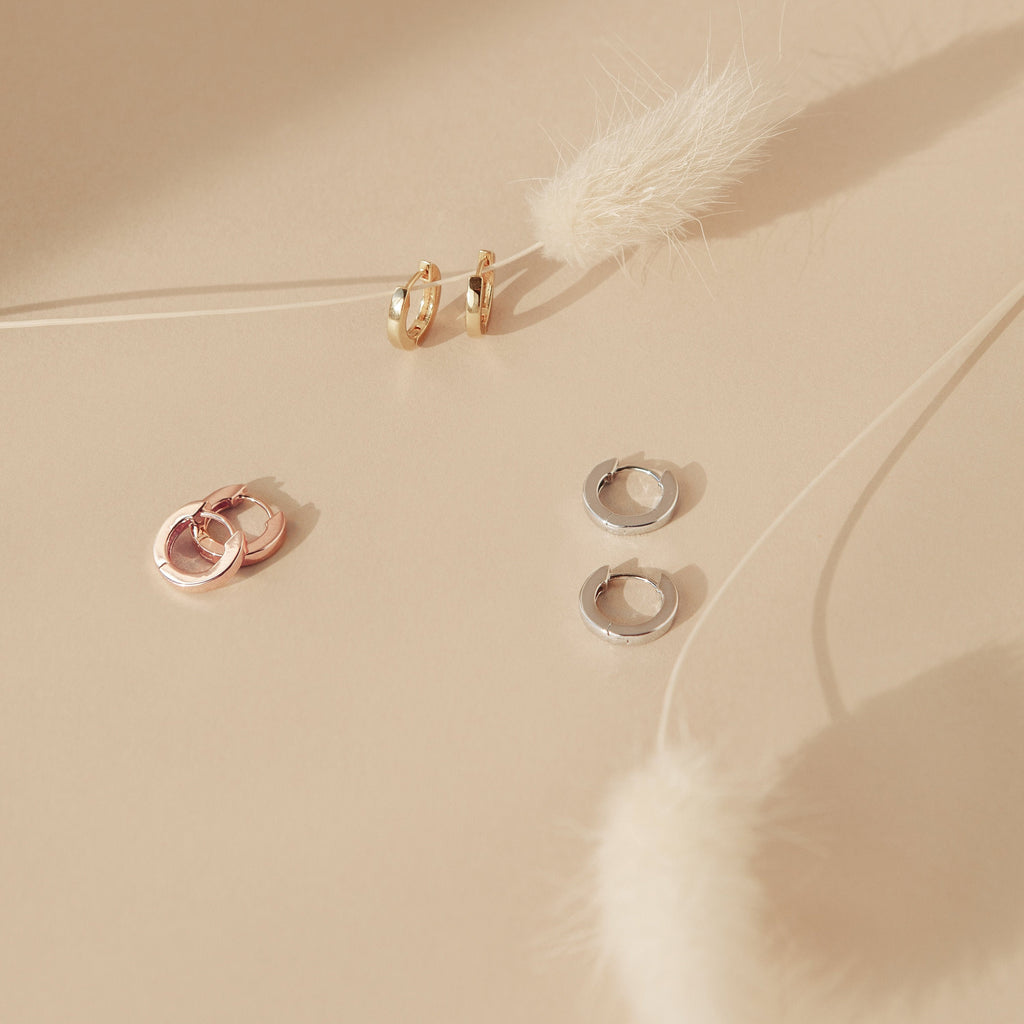 The Editor Huggies in Rose Gold rest on a beige surface with dried white grasses, bringing a minimal and elegant aesthetic.