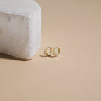 The Dainty Opal Earrings Set features gold hoops with white stones, displayed next to a white stone block on a beige background—ideal for those who love a delicate earrings look.