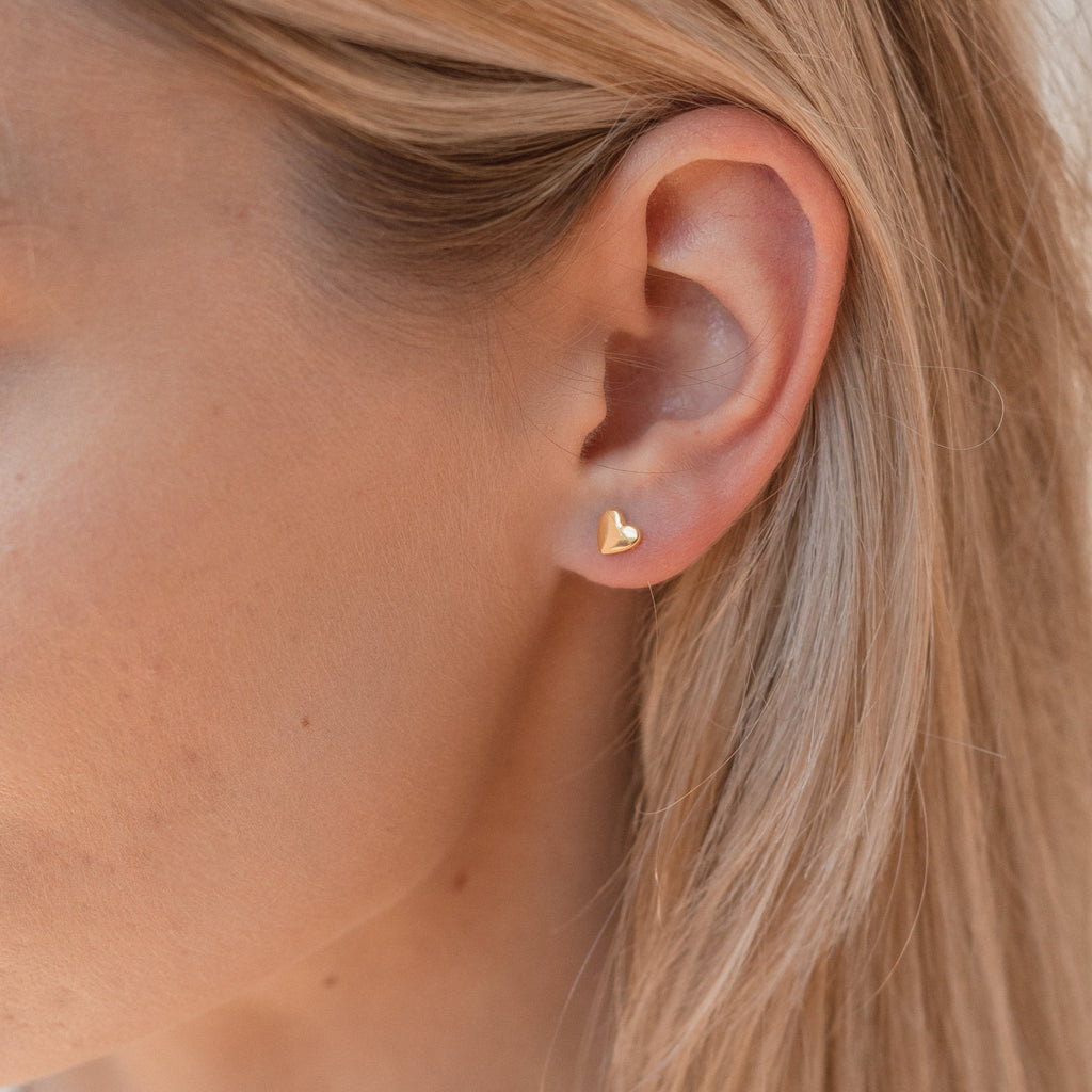 Close-up of a model wearing a gold heart-shaped earring with blonde hair.