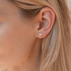Close-up of a model wearing a gold heart-shaped earring with blonde hair.