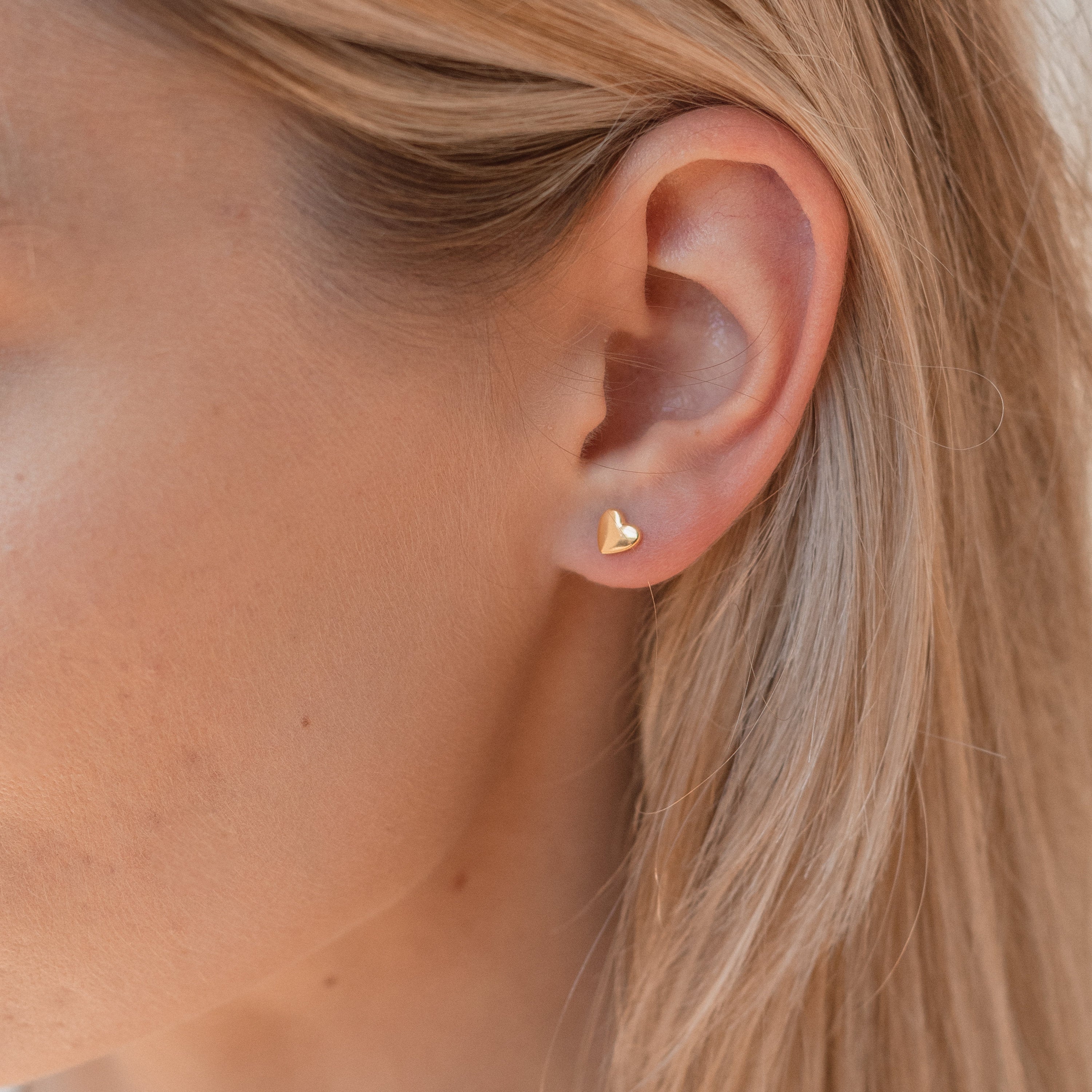 Close-up of a model wearing a gold heart-shaped earring with blonde hair.