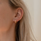 Close-up of a person with blonde hair wearing Thea Twisted Huggies—small gold hoop earrings—styled with minimalist pieces for a simple yet stylish ear stack.