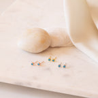 Set of gold, silver and rose gold stud earrings with blue gemstones on a soft beige fabric background