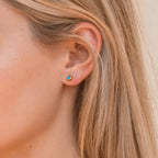 Close-up of a person wearing a colorful gold blue stud earring with blonde hair.