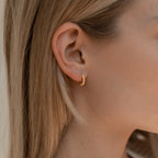 A close-up of a woman's ear adorned with Thea Twisted Huggies, highlighting her stylish ear stack.