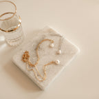 Gold and silver pearl link chain necklaces on a marble surface with a glass of water.