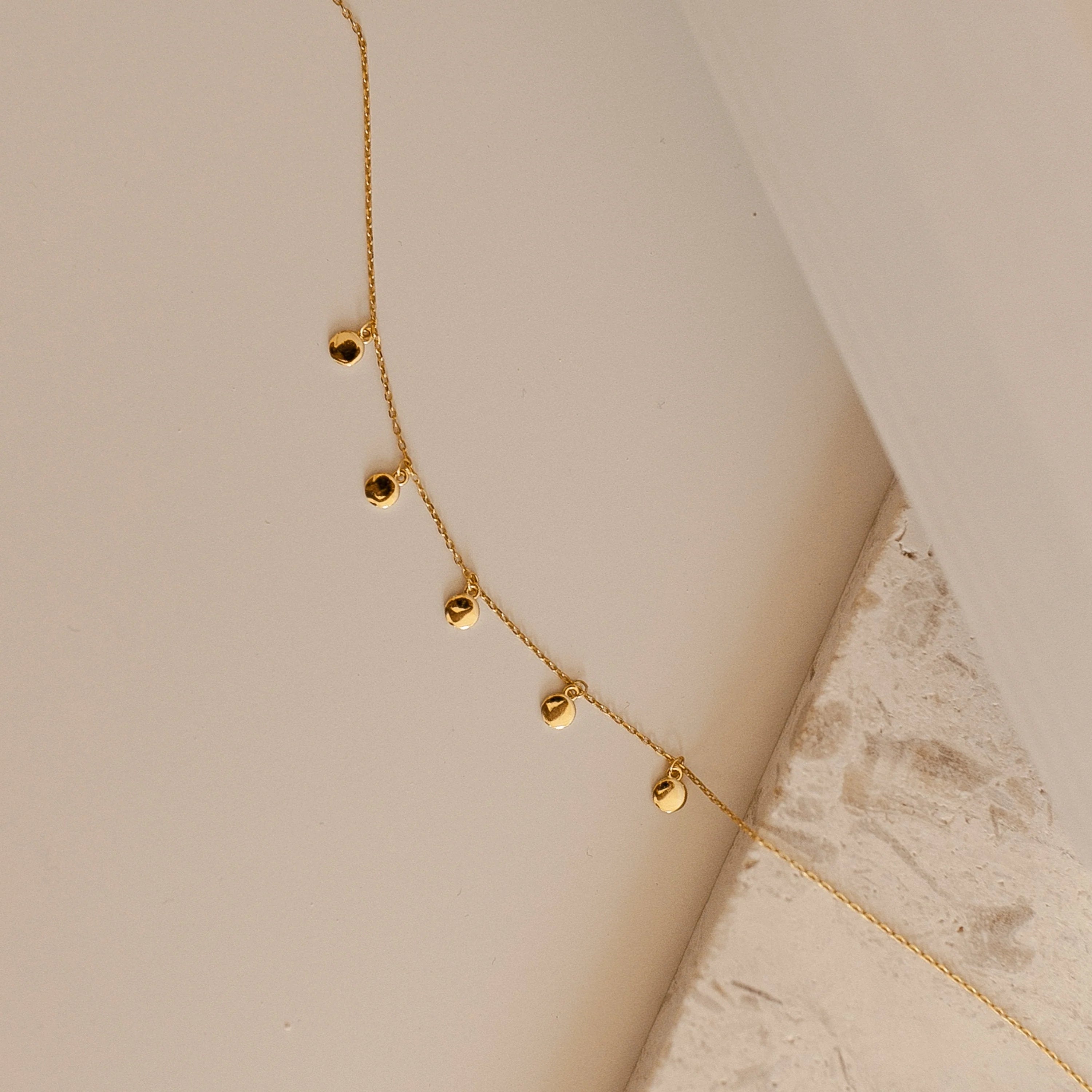The Onyx Necklace Set features delicate gold necklaces with small round charms, displayed on a neutral textured surface—ideal for layering and adding a subtle touch to your minimalist style.