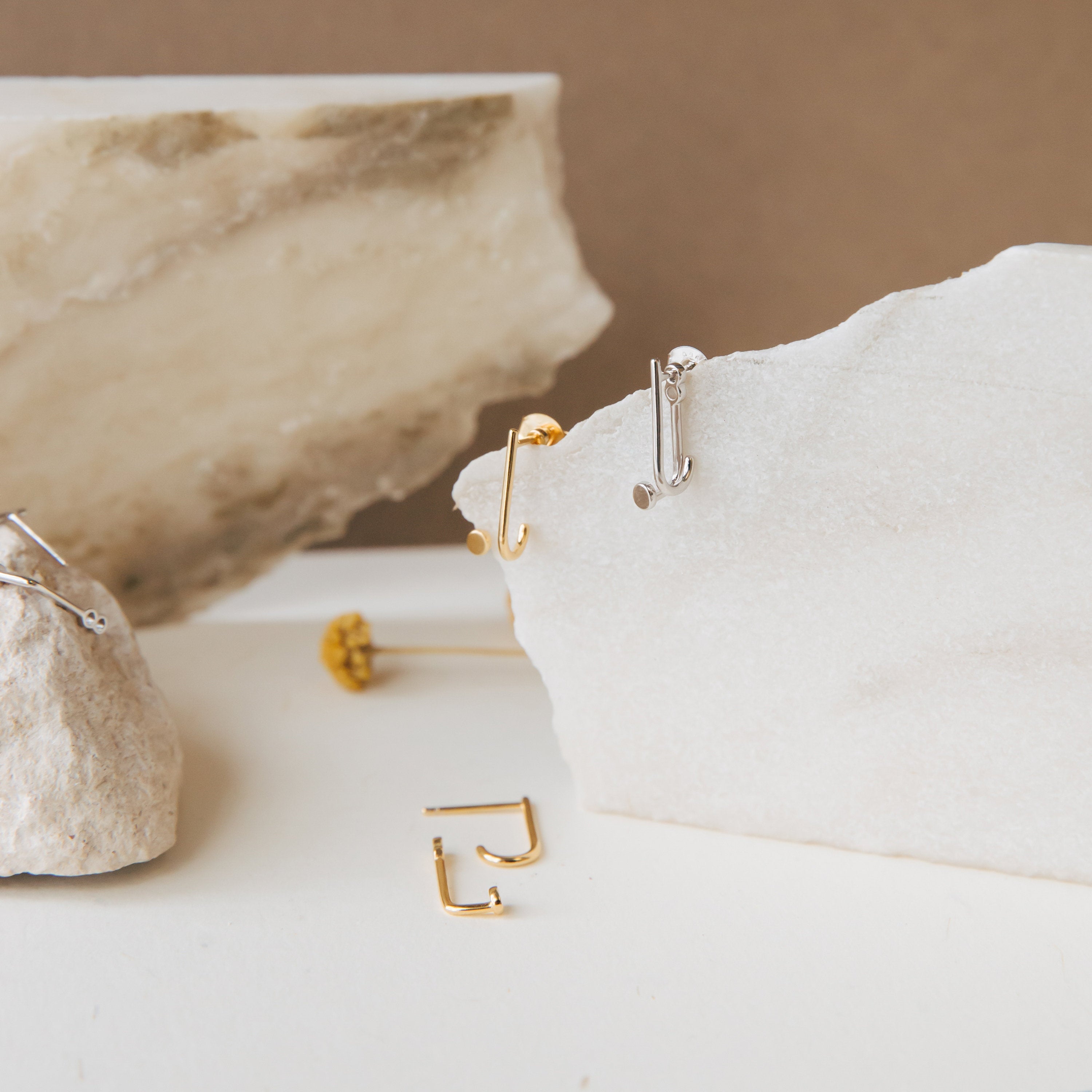 Gold and silver jacket earrings on a textured surface with a neutral background
