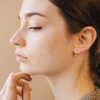 Close-up of a woman wearing gold jacket earrings with a neutral background