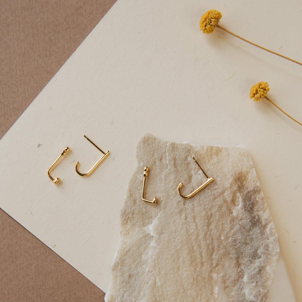 Gold jacket earrings on a stone surface with dried flowers in the background